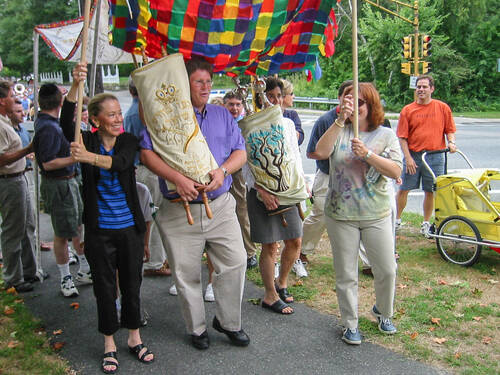 Image of marchers in procession holding Torahs under a multicolored chuppah.